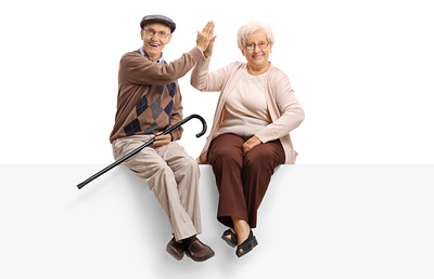 Elderly man and woman seated on a panel high-fiving each other and looking at the camera isolated on white background