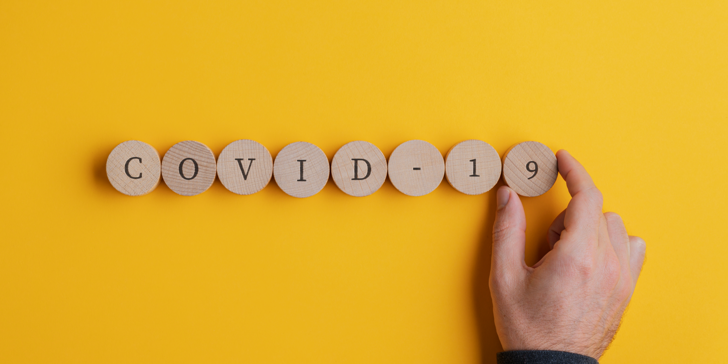 Auf Holzsteinen stehen Buchstaben. Mit den Buchstaben wurde das Wort 'Covid-19' gelegt.